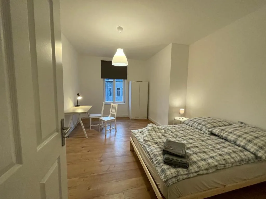 Doppelbett mit karierter Bettwäsche, Nachttisch und Schreibtisch im Zimmer der Pension Luisengrün