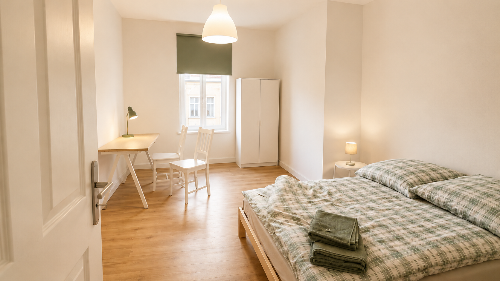 Helles Gästezimmer der Pension Luisengrün in Chemnitz mit Doppelbett, Holzboden, kleinem Tisch mit weißen Stühlen und weißem Schrank
